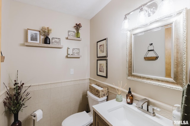 bathroom featuring vanity, wainscoting, toilet, and tile walls