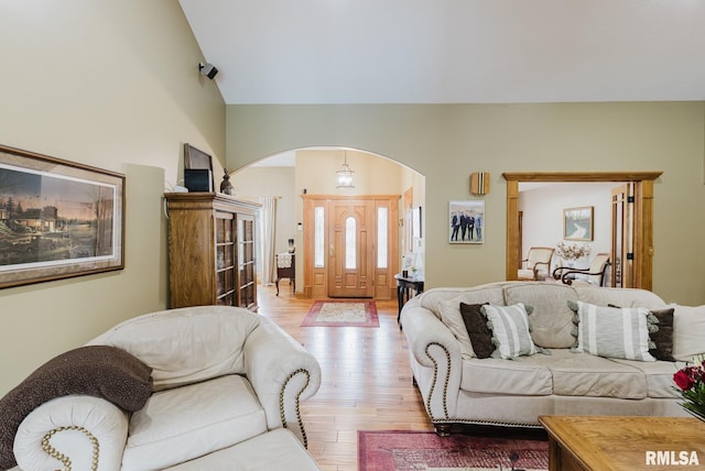 living room with arched walkways, light wood-style flooring, and lofted ceiling