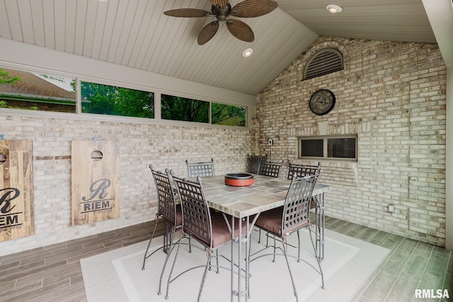 dining area featuring wood tiled floor, ceiling fan, lofted ceiling, and brick wall