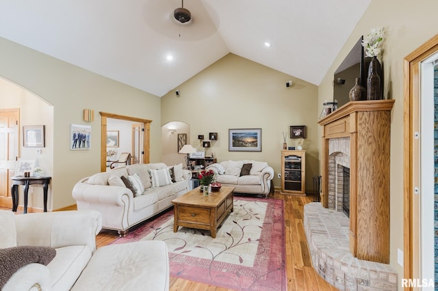 living area featuring light wood finished floors, a fireplace, arched walkways, high vaulted ceiling, and wine cooler