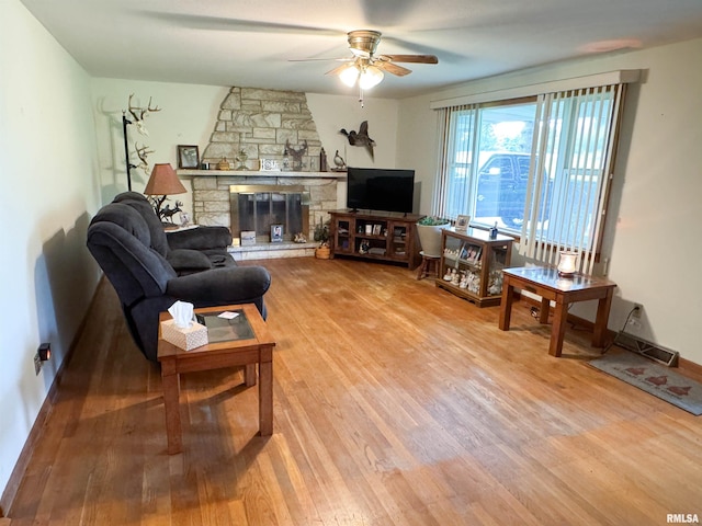 living area with a ceiling fan, baseboards, a stone fireplace, and light wood-style flooring