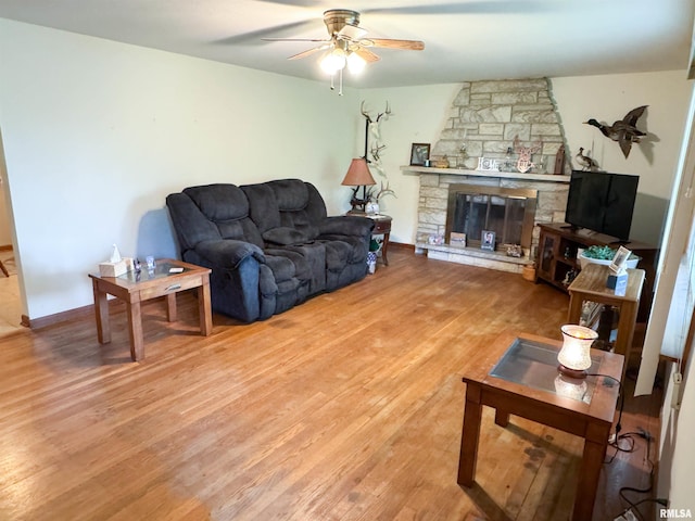 living area with a stone fireplace, a ceiling fan, and wood finished floors