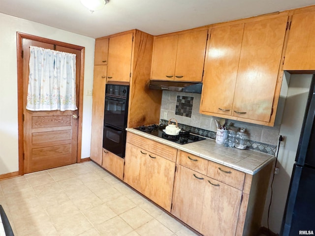 kitchen featuring tile countertops, baseboards, decorative backsplash, under cabinet range hood, and black appliances