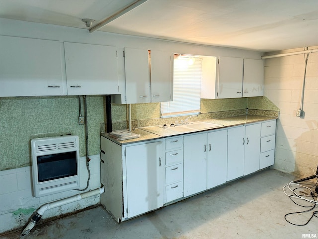 kitchen with white cabinets, a sink, concrete block wall, heating unit, and unfinished concrete floors