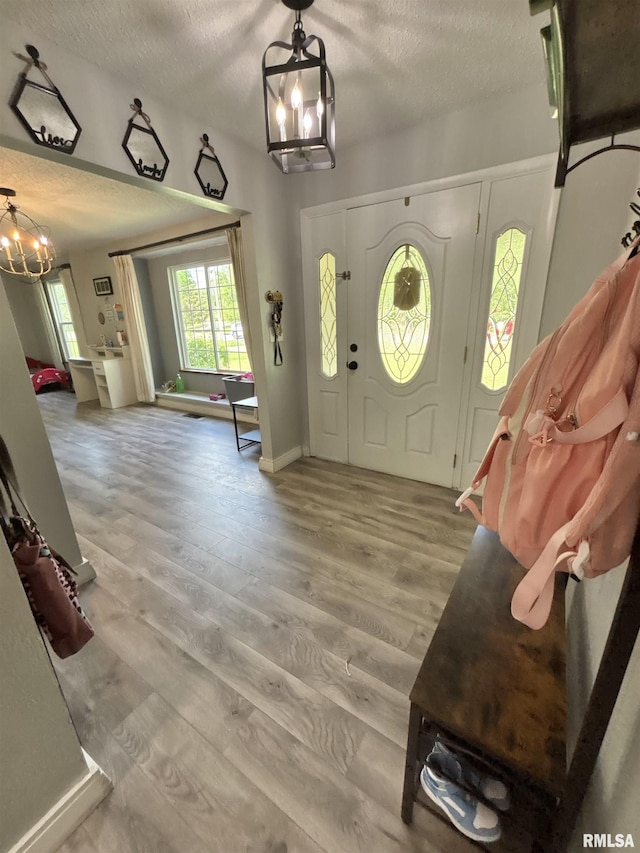 entryway featuring an inviting chandelier, baseboards, light wood-type flooring, and a textured ceiling