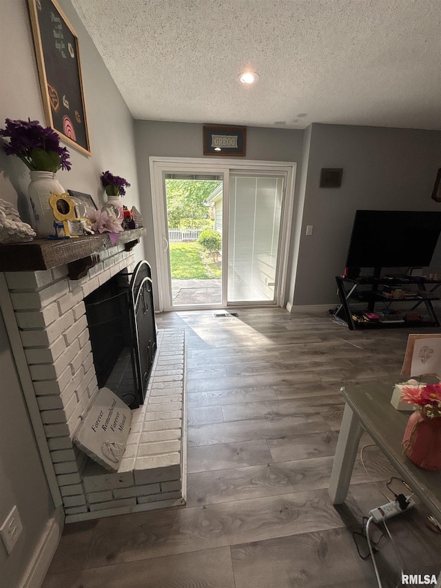 living area featuring baseboards, a textured ceiling, wood finished floors, and a fireplace