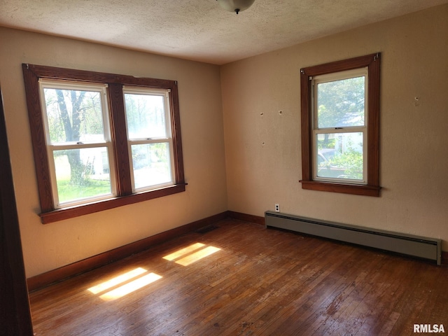 empty room featuring baseboard heating, hardwood / wood-style flooring, a textured ceiling, and a wealth of natural light