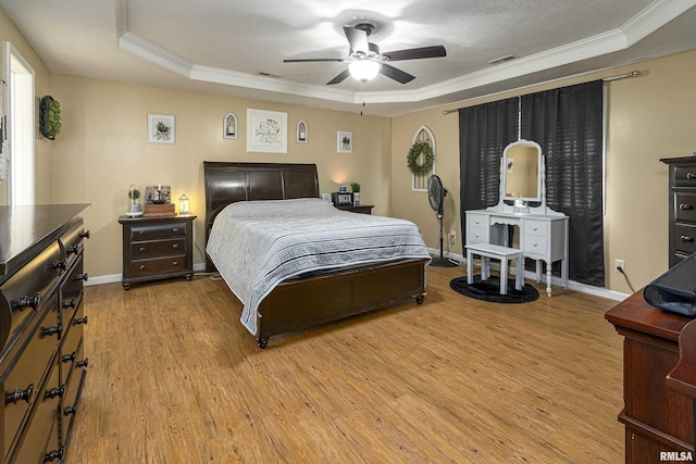 bedroom featuring crown molding, visible vents, baseboards, a raised ceiling, and light wood-style floors