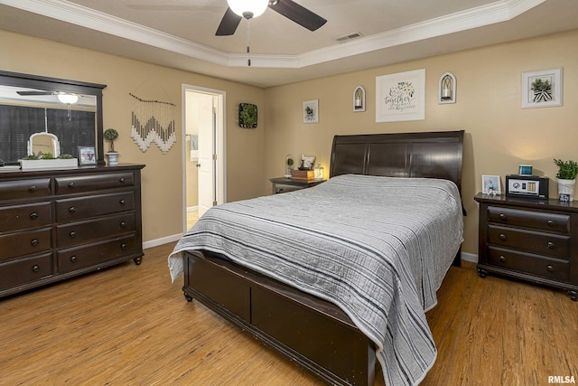 bedroom featuring light wood-type flooring, visible vents, a raised ceiling, and ornamental molding