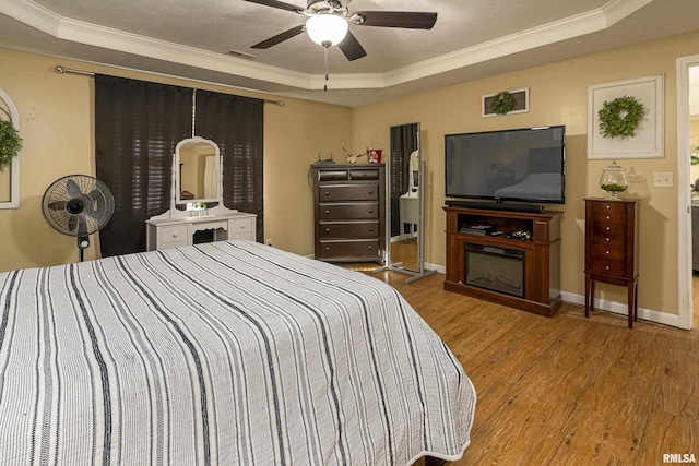 bedroom featuring baseboards, ornamental molding, visible vents, wood finished floors, and a raised ceiling