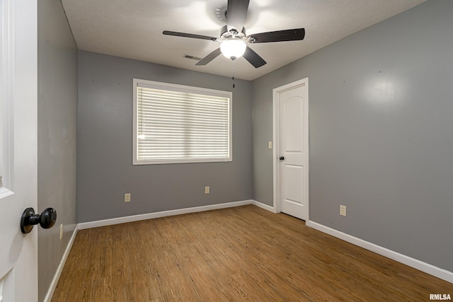 empty room featuring a ceiling fan, baseboards, visible vents, and wood finished floors