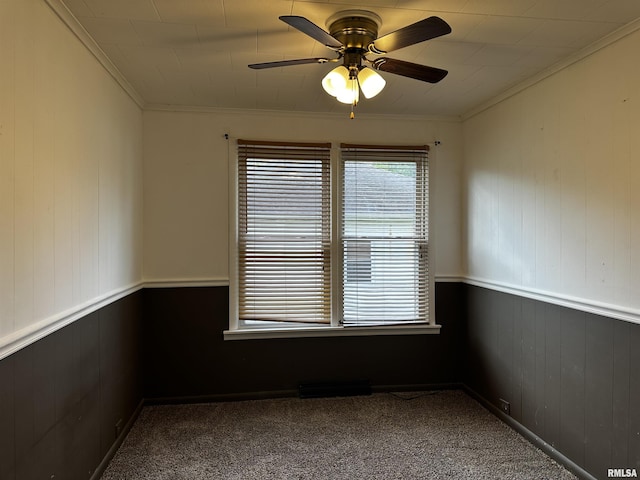 empty room with carpet flooring, ornamental molding, wooden walls, and ceiling fan