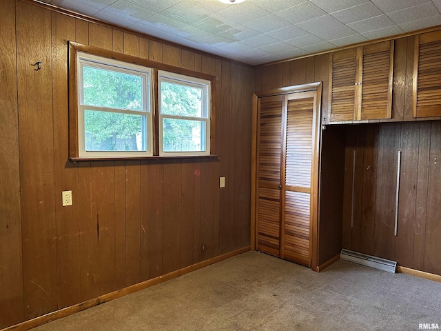 unfurnished bedroom with light carpet, wooden walls, a baseboard radiator, and a closet