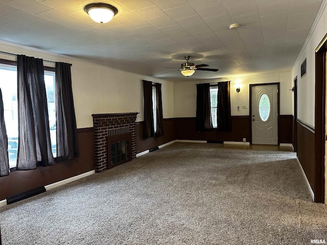 unfurnished living room with carpet, a ceiling fan, a fireplace, and a wainscoted wall