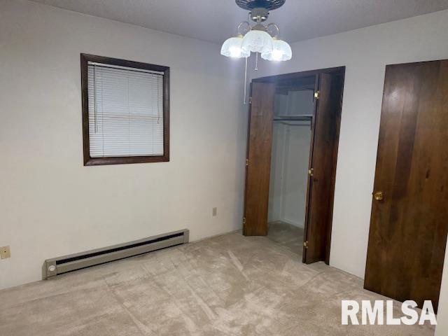 unfurnished bedroom with light carpet, a baseboard radiator, multiple closets, and a notable chandelier
