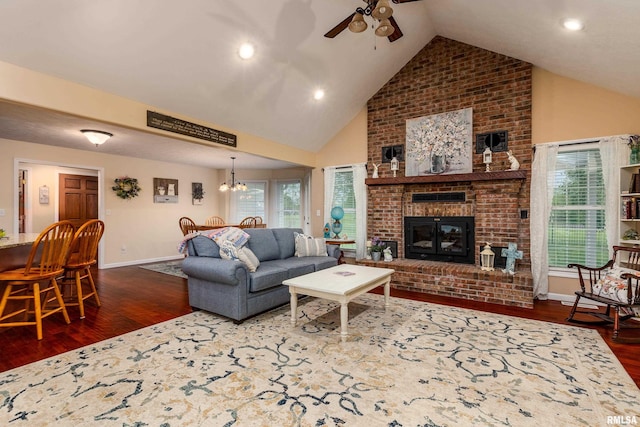 living area featuring ceiling fan with notable chandelier, high vaulted ceiling, a fireplace, dark wood-style floors, and baseboards