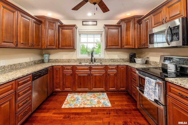 kitchen with a ceiling fan, a sink, appliances with stainless steel finishes, light stone counters, and dark wood-style floors