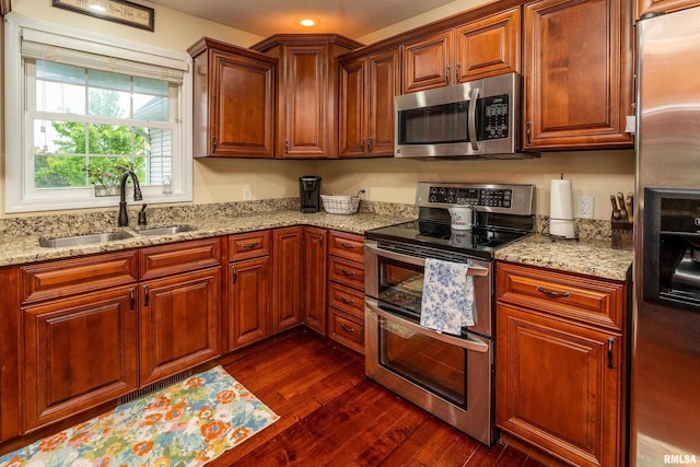 kitchen featuring dark wood-style flooring, light stone counters, stainless steel appliances, and a sink