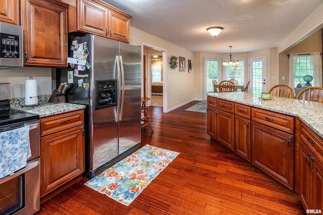kitchen with appliances with stainless steel finishes, brown cabinetry, dark wood-style floors, and a notable chandelier