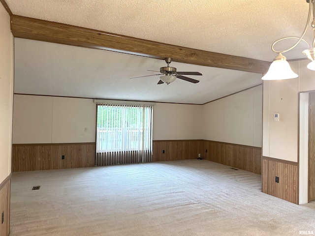 carpeted empty room featuring a wainscoted wall, a ceiling fan, lofted ceiling with beams, and a textured ceiling