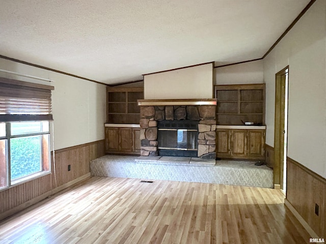 unfurnished living room featuring wood finished floors, crown molding, wood walls, wainscoting, and lofted ceiling
