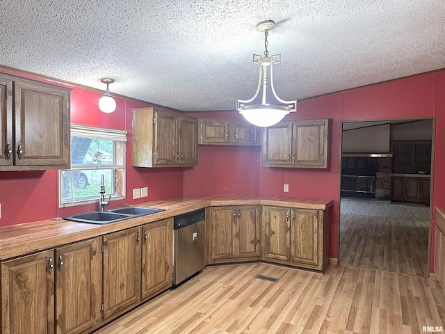 kitchen featuring a textured ceiling, brown cabinetry, a sink, and dishwasher