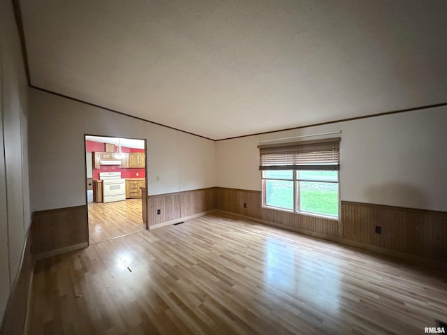 unfurnished room with a wainscoted wall, vaulted ceiling, wood finished floors, and wooden walls
