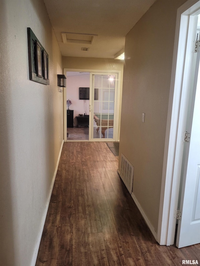 hallway featuring dark wood-style flooring, attic access, baseboards, and visible vents