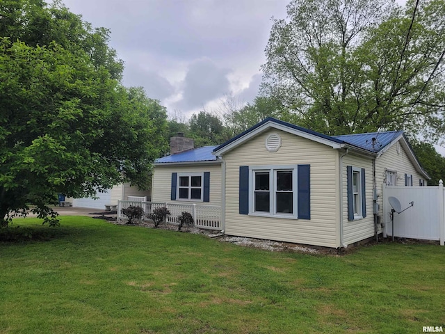 back of house featuring a chimney, metal roof, and a yard