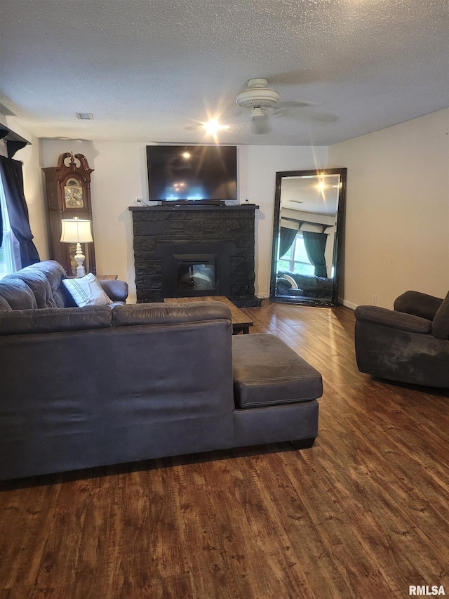 living area with a textured ceiling, a stone fireplace, visible vents, ceiling fan, and wood finished floors