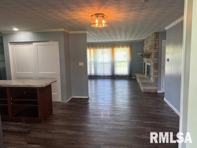 unfurnished living room featuring ornamental molding, baseboards, a stone fireplace, and dark wood finished floors