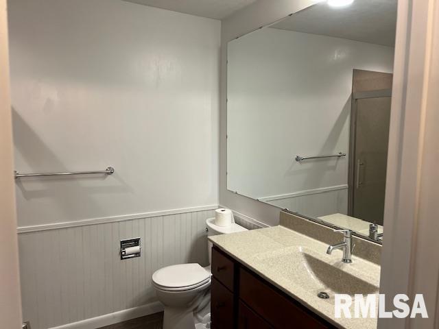 full bathroom with a shower with door, vanity, toilet, and a wainscoted wall