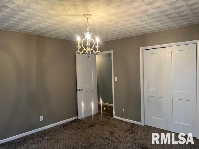 unfurnished dining area featuring a chandelier, a textured ceiling, carpet flooring, and baseboards