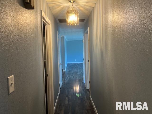 corridor featuring a textured wall, dark wood-type flooring, and a notable chandelier