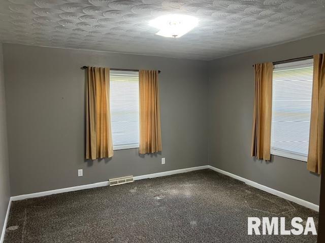 empty room featuring a textured ceiling, baseboards, and visible vents