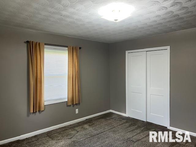 unfurnished bedroom with baseboards, a closet, dark colored carpet, and a textured ceiling