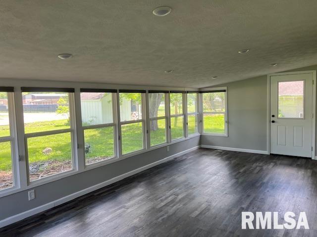 unfurnished sunroom featuring wood finished floors, baseboards, and a healthy amount of sunlight