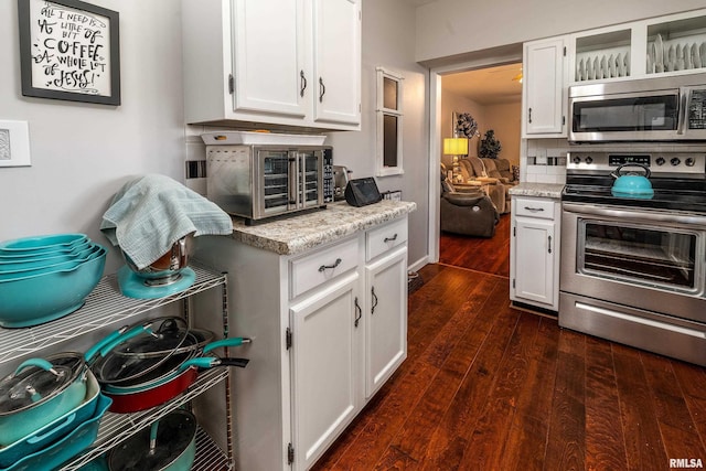 kitchen with appliances with stainless steel finishes, white cabinetry, dark wood-type flooring, and light stone countertops
