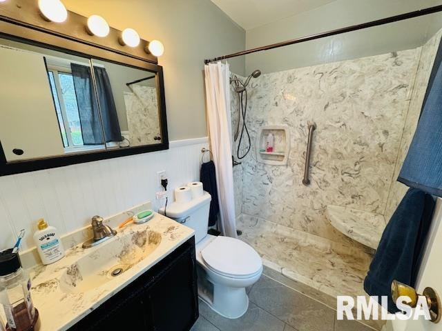 full bathroom with tiled shower, toilet, vanity, tile patterned flooring, and a wainscoted wall