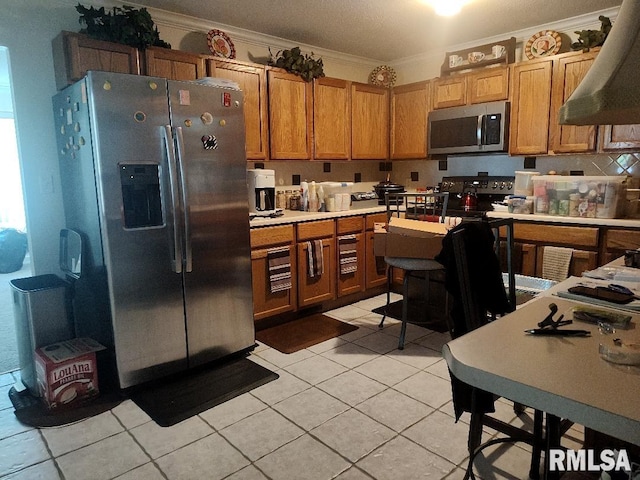 kitchen with stainless steel appliances, ornamental molding, light tile patterned floors, light countertops, and brown cabinets