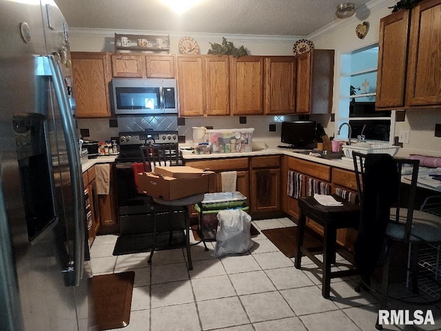 kitchen with appliances with stainless steel finishes, ornamental molding, light countertops, a sink, and light tile patterned floors