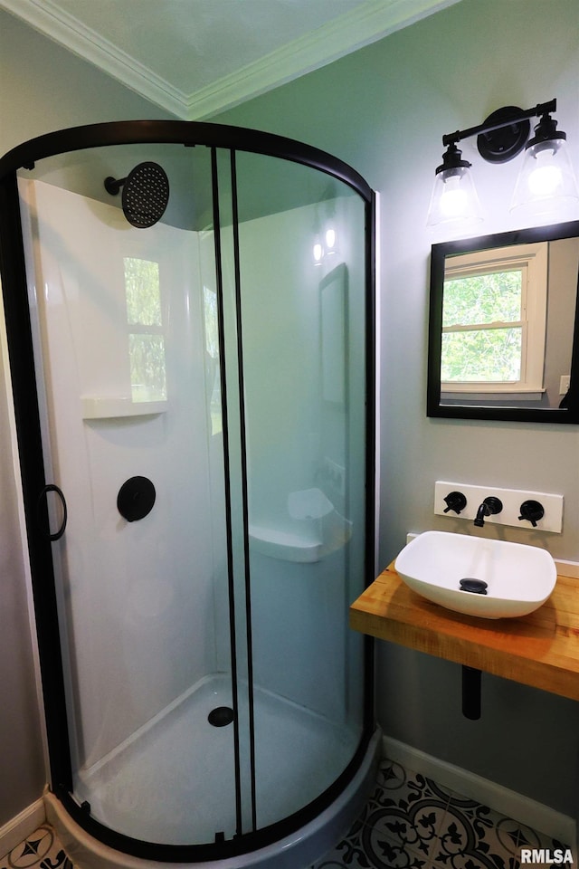 bathroom with a shower stall, crown molding, a sink, baseboards, and tile patterned flooring
