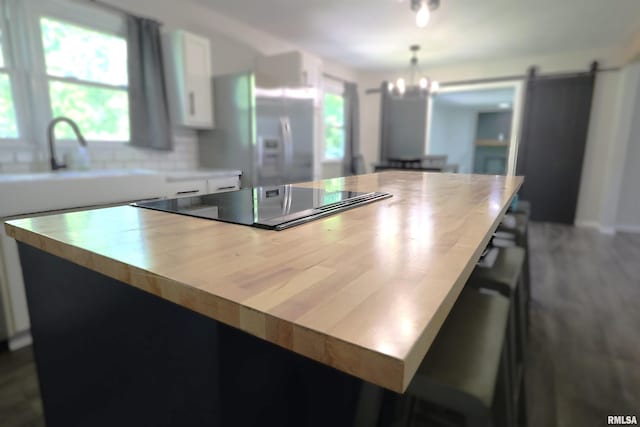 kitchen with stainless steel refrigerator with ice dispenser, black electric cooktop, white cabinets, backsplash, and a center island