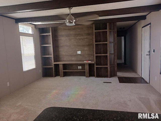 unfurnished living room featuring healthy amount of natural light, beam ceiling, carpet, and a ceiling fan