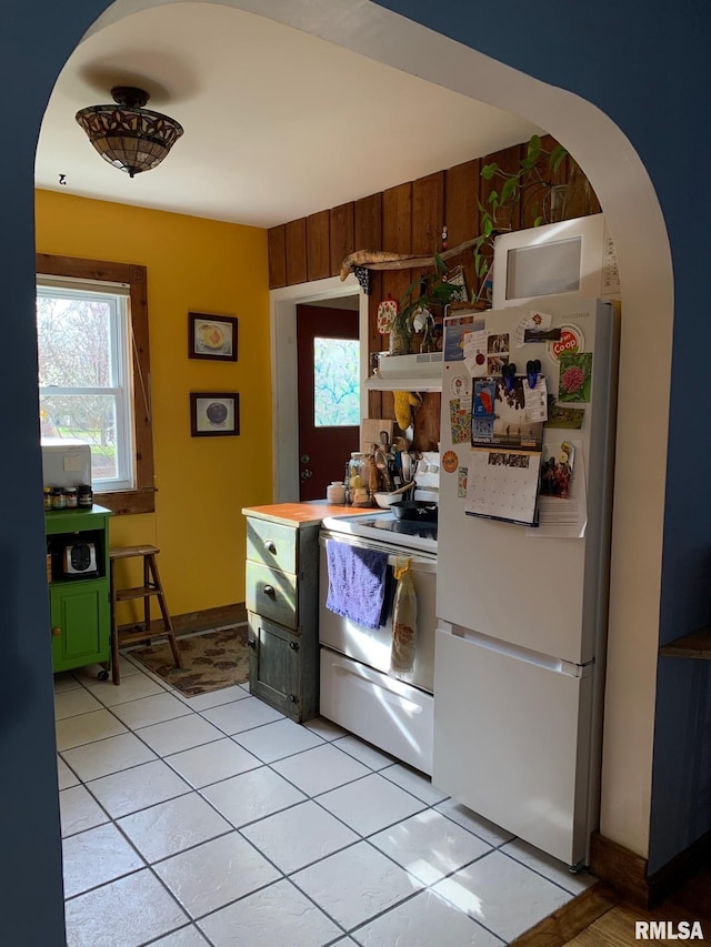 kitchen featuring white appliances, under cabinet range hood, light tile patterned floors, arched walkways, and baseboards