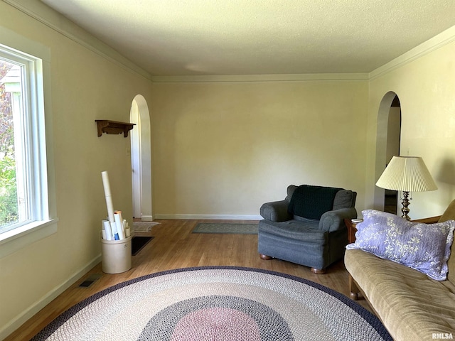 living room with arched walkways, wood finished floors, baseboards, crown molding, and a textured ceiling