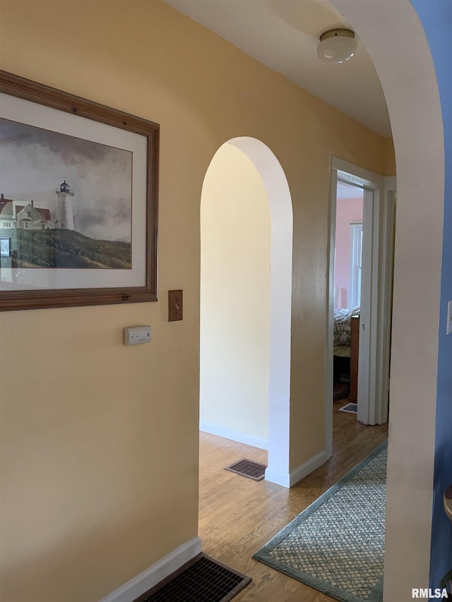 hallway with arched walkways, wood finished floors, and baseboards