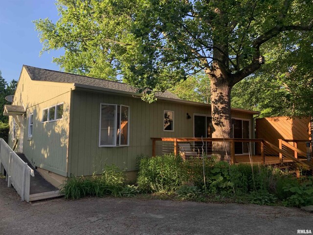 view of front of house with fence, a deck, and roof with shingles