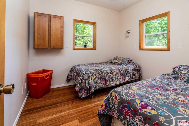 bedroom with multiple windows, wood finished floors, and baseboards