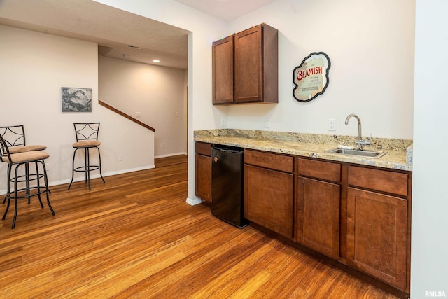 kitchen with a sink, light wood finished floors, light stone countertops, and baseboards